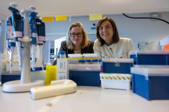 a blonde woman and a brunet woman beside each other in a lab