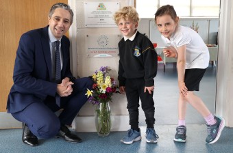 Minister Simon Harris TD meeting with two primary school students with a vase of flowers in-between them