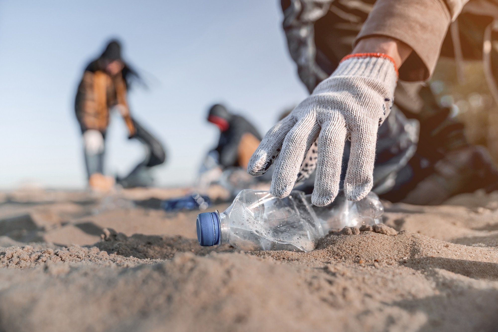 gloved hand picking up a crushed plastic bottle from a beach