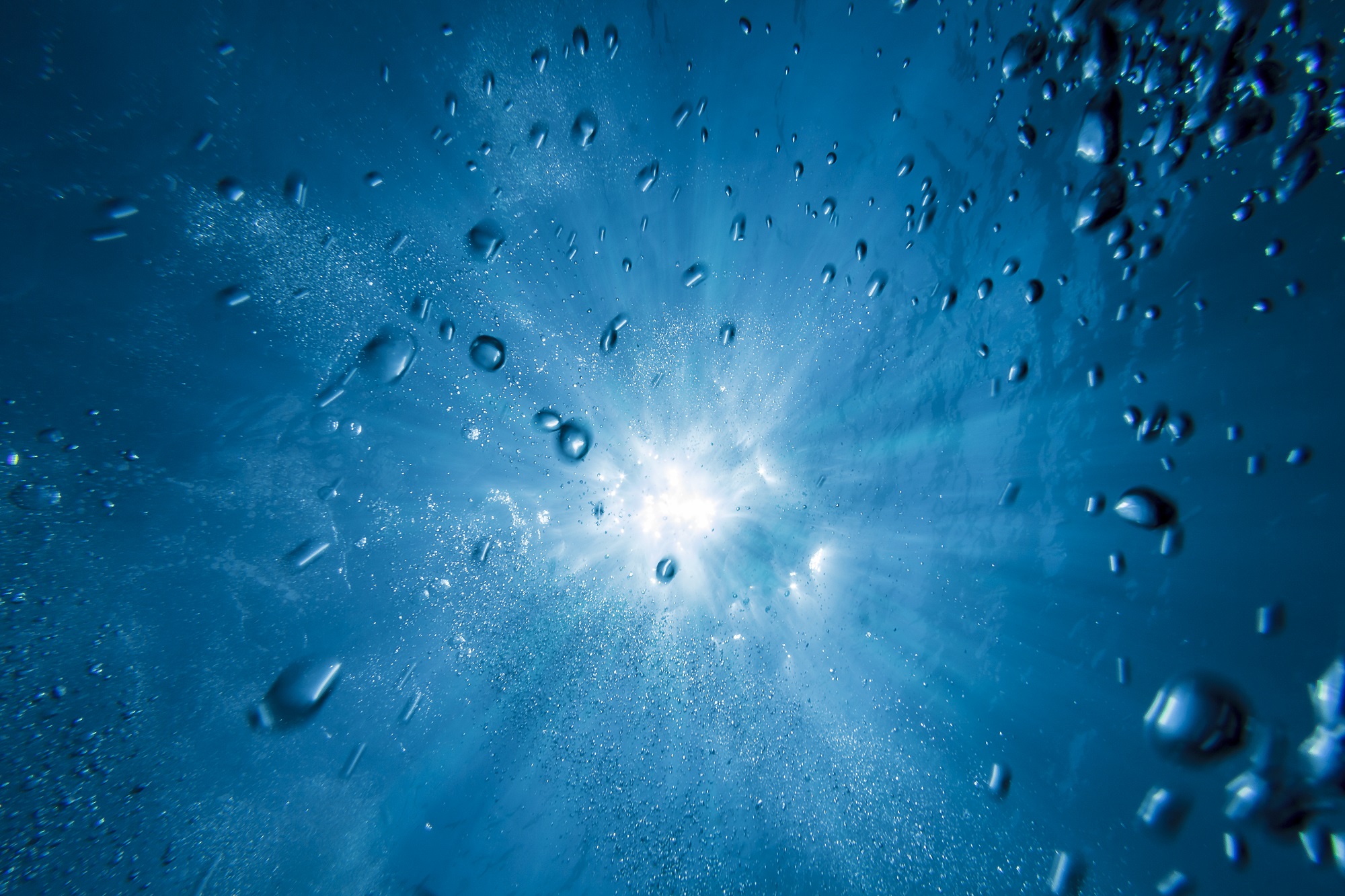 image of sunlight seen from below water with bubbles in it  