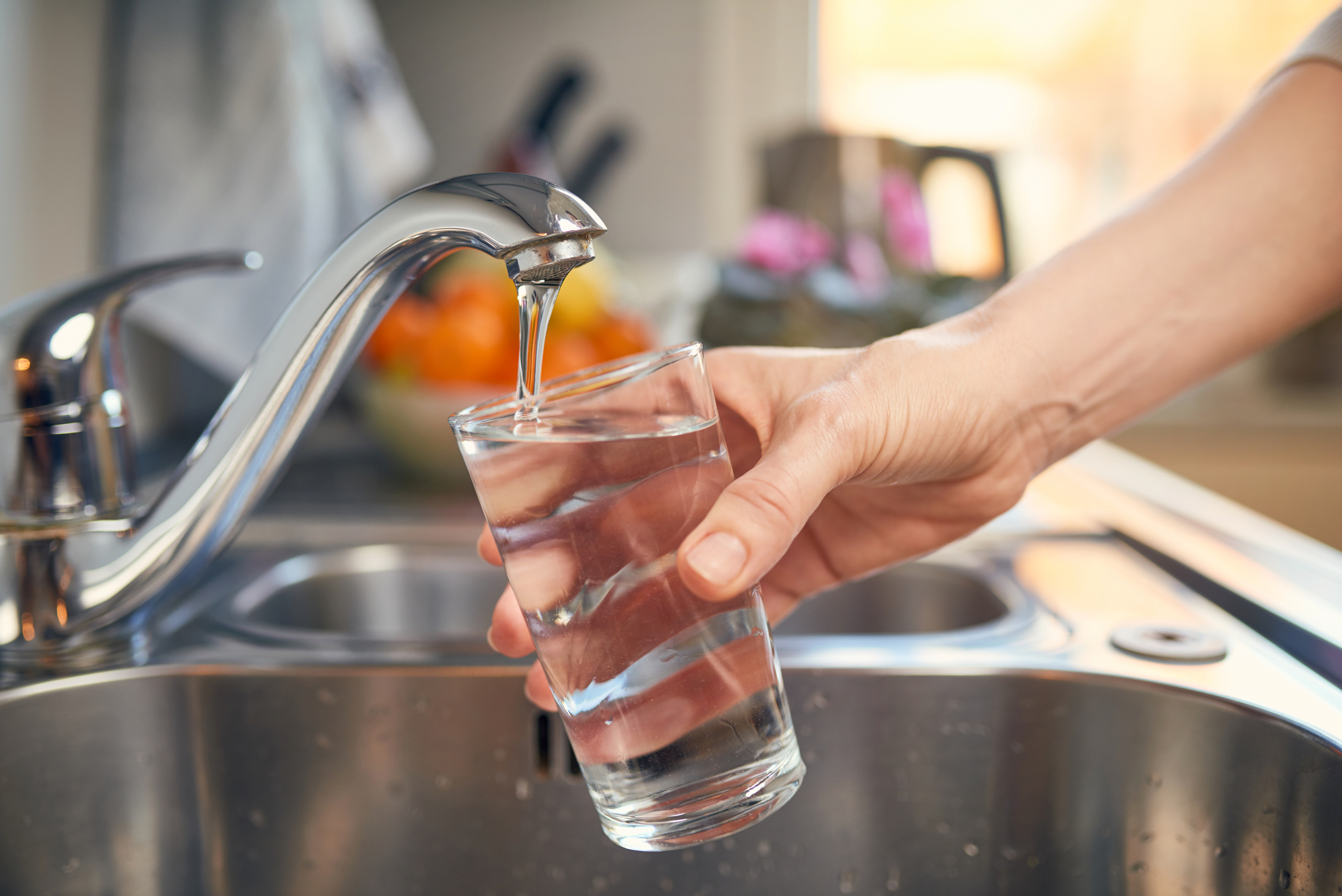 person filling a glass with water from a tap at home