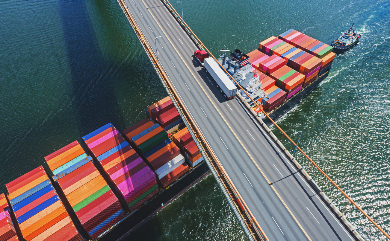 composite image of a container ship passing under a road bridge with an articulated lorry on it