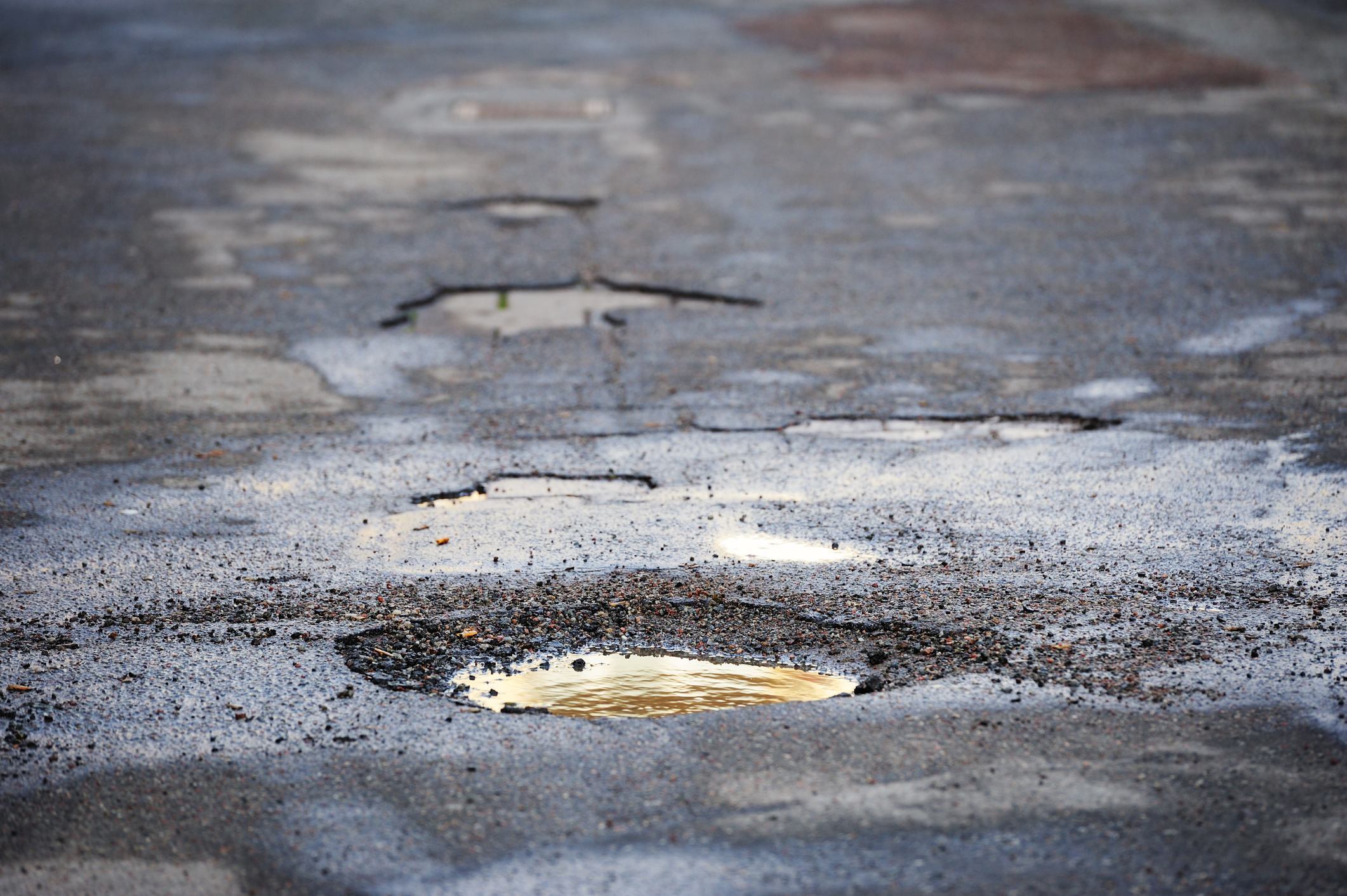 a cluster of potholes in a road with small puddle in one of them