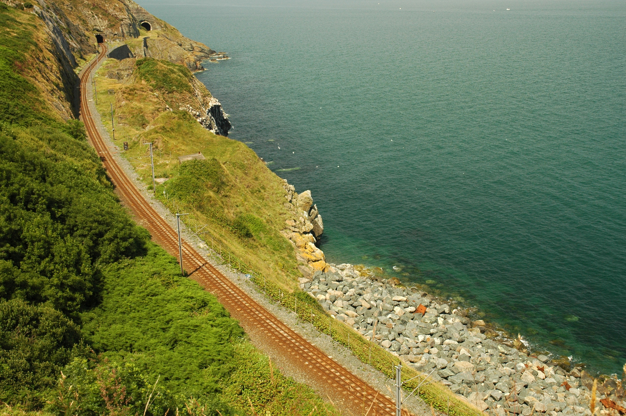 photograph of railway line running between hillside and sea