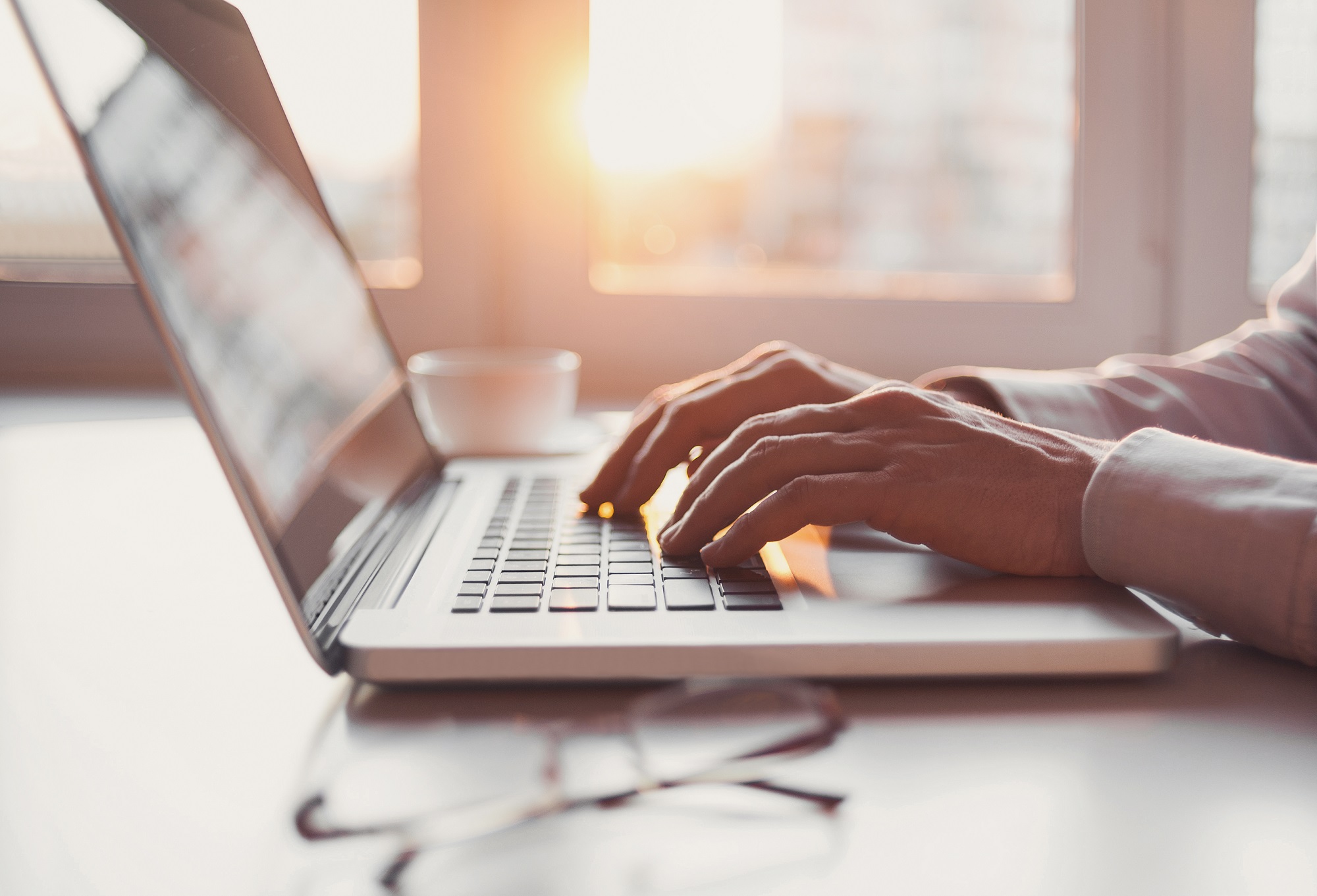 a person typing on a laptop with the sun setting in the city behind