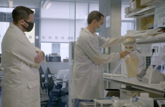 two men dressed in lab coats working on an experiment in a lab