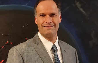 An Image of Dan Kilper in a white shirt, agrey coat and a blue tie
