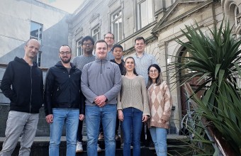 Image of 9 people standing on steps outside a stone building. 