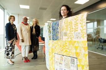 Image of a woman holding a patterned textile with three women standing on the background