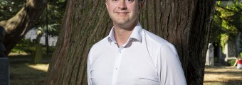 A headshot of a man wearing a shirt standing in front of a tree.