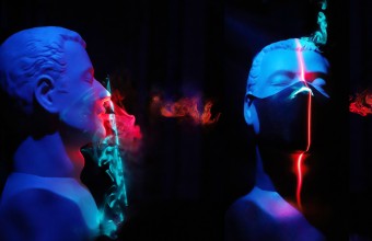 Statues of three male men amongst a dark background with blue and red lighting