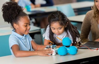 Two young girls in classroom looking interested at an experiment.