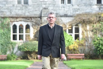 A man wearing glasses dressed professional walking outside a old building