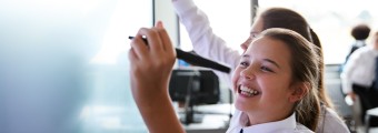 Image of a young female student smiling writing on white board at school