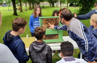 Many children and bee keeper standing looking and pointing at bees in their bee home