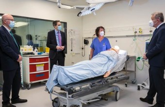 Fake Patient lying in hospital bed with a nurse and three men in the same room