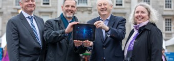 three men and a women holding up an ipad outside in front of a historical building.