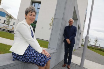 An image of a woman sitting down on a raised surface and a man standing next to a wall behind the woman