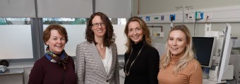 Image of 4 women standing together looking at a screen 