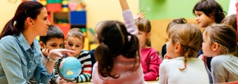 Teacher showing a globe to her class with one hand raised by a student