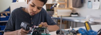 A boy is sitting at his work bench as he builds a structure as part of his engineering activity