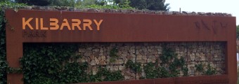 An iron Kilbarry sign on a stone wall outside the park