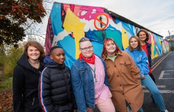 Many young people standing in front of graffiti art on a building