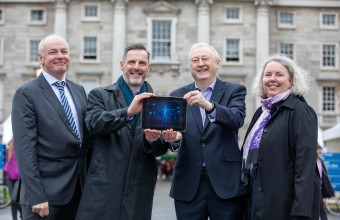 three men and a women holding up an ipad outside in front of a historical building.