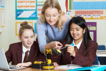 Teacher is showing two students how to fix/set up a mini robotic arm