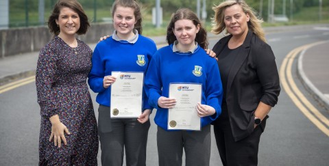 Image of 2 women and 2 girls standing outdoors. The girls are wearing school uniforms and holding certificates. 