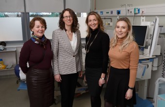 Image of 4 women standing together looking at a screen 