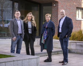 2 women and 2 men standing outside a red brick building with glass door.