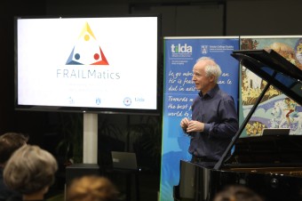 Older man on stage presenting using a screen