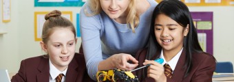 A teacher showing two students how to fix or set up a mini robotic arm 