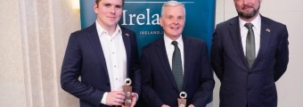Three men dressed in suits while two of the men are holding trophies