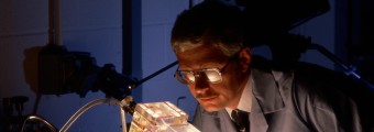 A person in a lab wearing a lab coat looking at a glowing object