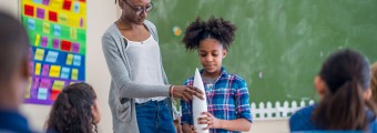 A teacher and student holding a white rocket ship at the front of the classroom