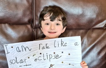 Young boy Adam king holding up drawn  poster saying "i am rare like a solar eclipse".