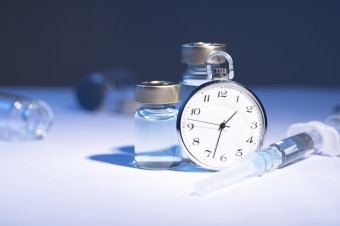 Image of small glass vials, containing clear liquid; a clock; and a syringe