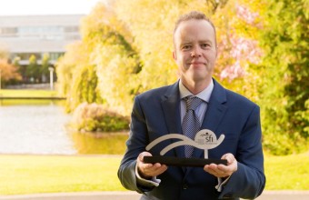 An image of Professor William Gallagher, standing in front of a large tree, holding the SFI Reseacher of the Year trophy