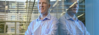 Brian Corbett from Tyndall National Institute standing up against a glass wall mirroring his reflect.