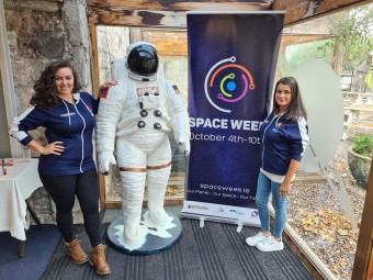 Photo of two brunet girls standing beside a statue of an astronaut