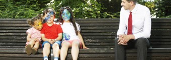 Three young children sitting on a bench at the festival of curiosity with their faces painted talking to a older man 