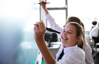 Student smiling as she writes on the chalkboard