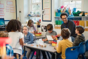 Teacher laughing with students as they cut up plastic for supplies