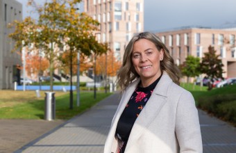 Image of Dr Katriona O'Sullivan standing outdoors in Maynooth University campus. There are buildings and trees in the background. 