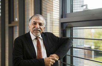 A older man leading up against a window wearing a suit