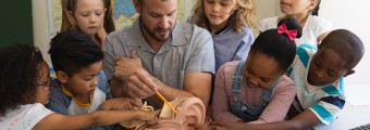 A teacher showing a plastic modal ear to students as they crowd around him to look