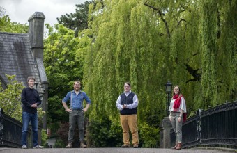 Four people standing on a bridge in a rural setting