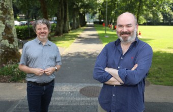 Two men standing in a bright green outdoor area 